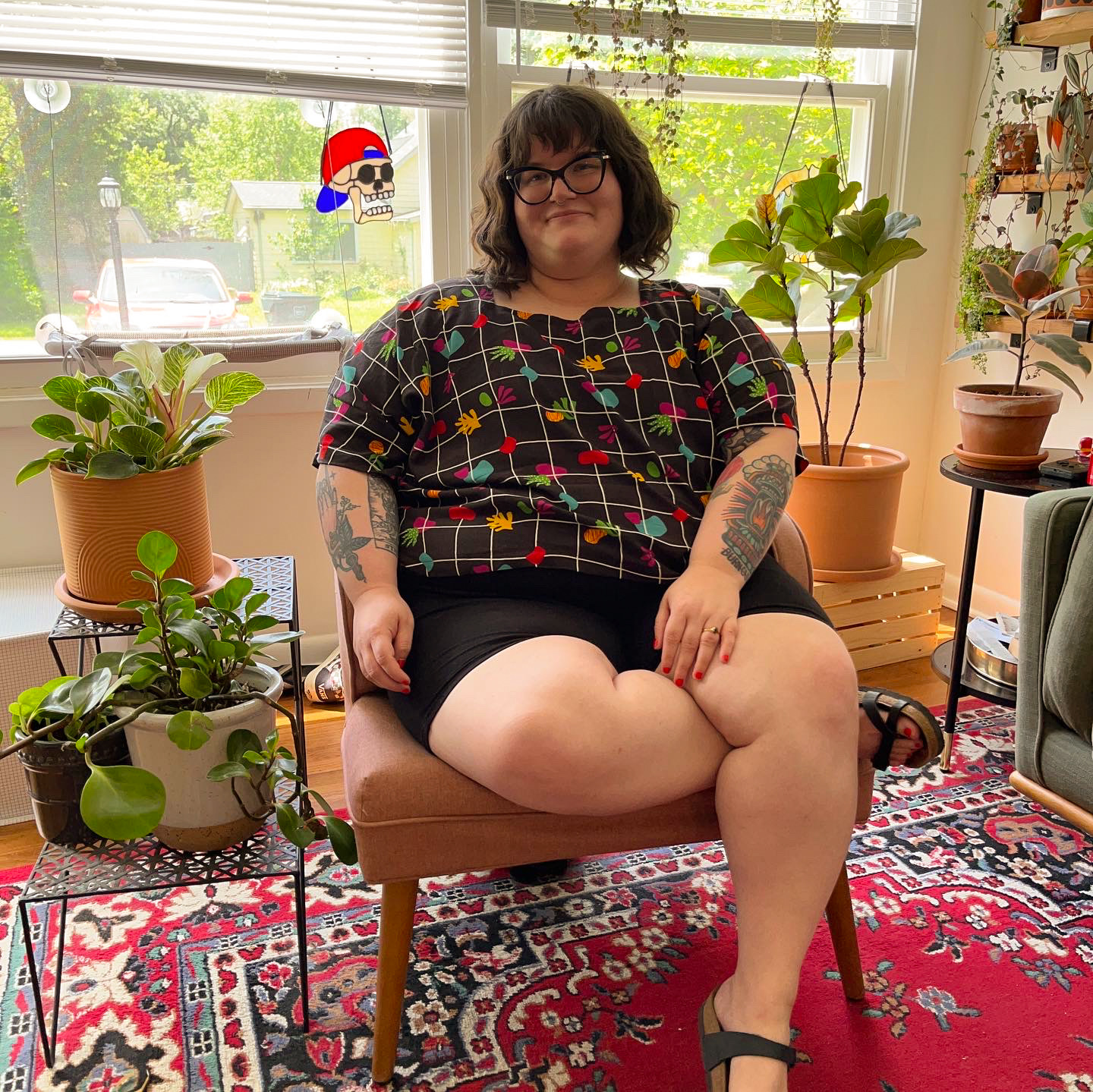 A photo of a woman, Kenzie, sitting in a chair surrounded by plants.